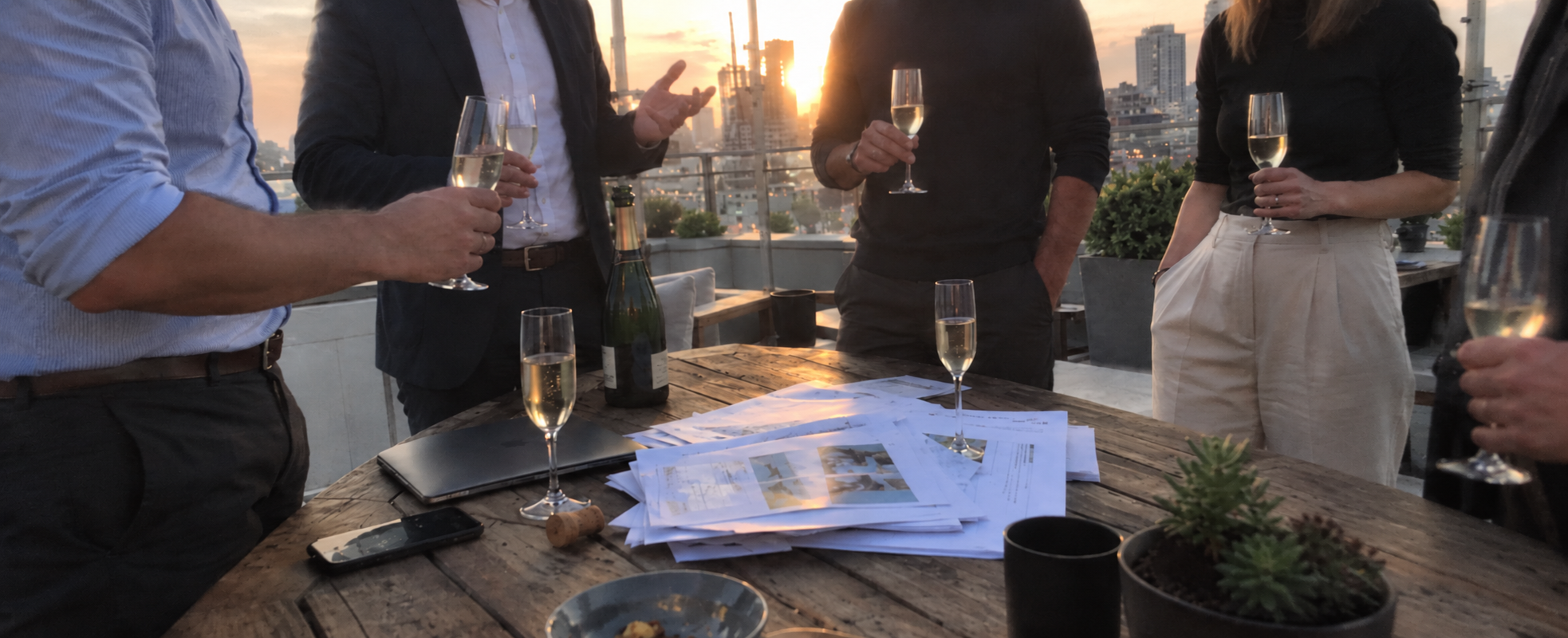 A team sharing website plans and documents around a terrace table at sunset