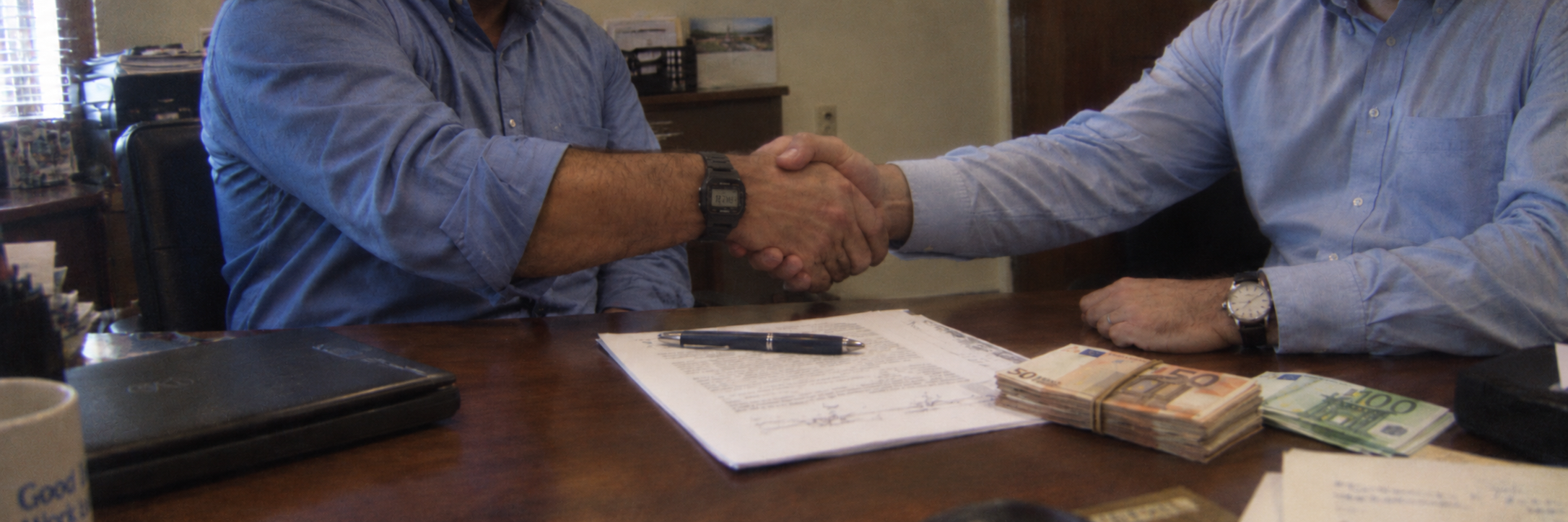 Two people shaking hands over an agreement at a desk.